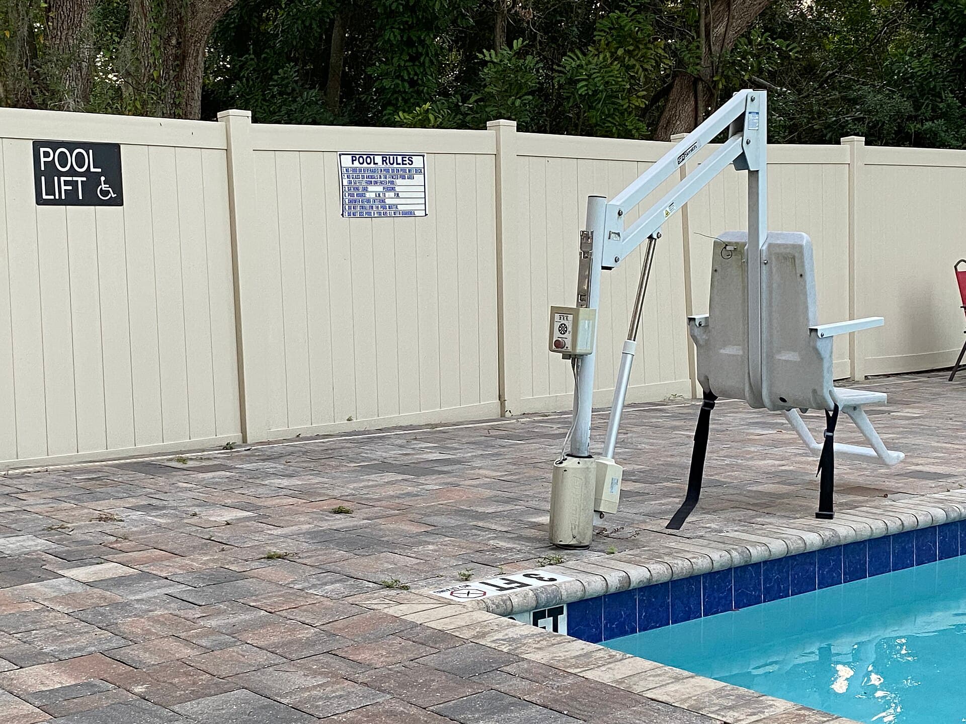 ADA-compliant accessible pool lift chair at the edge of a pool, next to a 'Pool Lift' accessibility sign