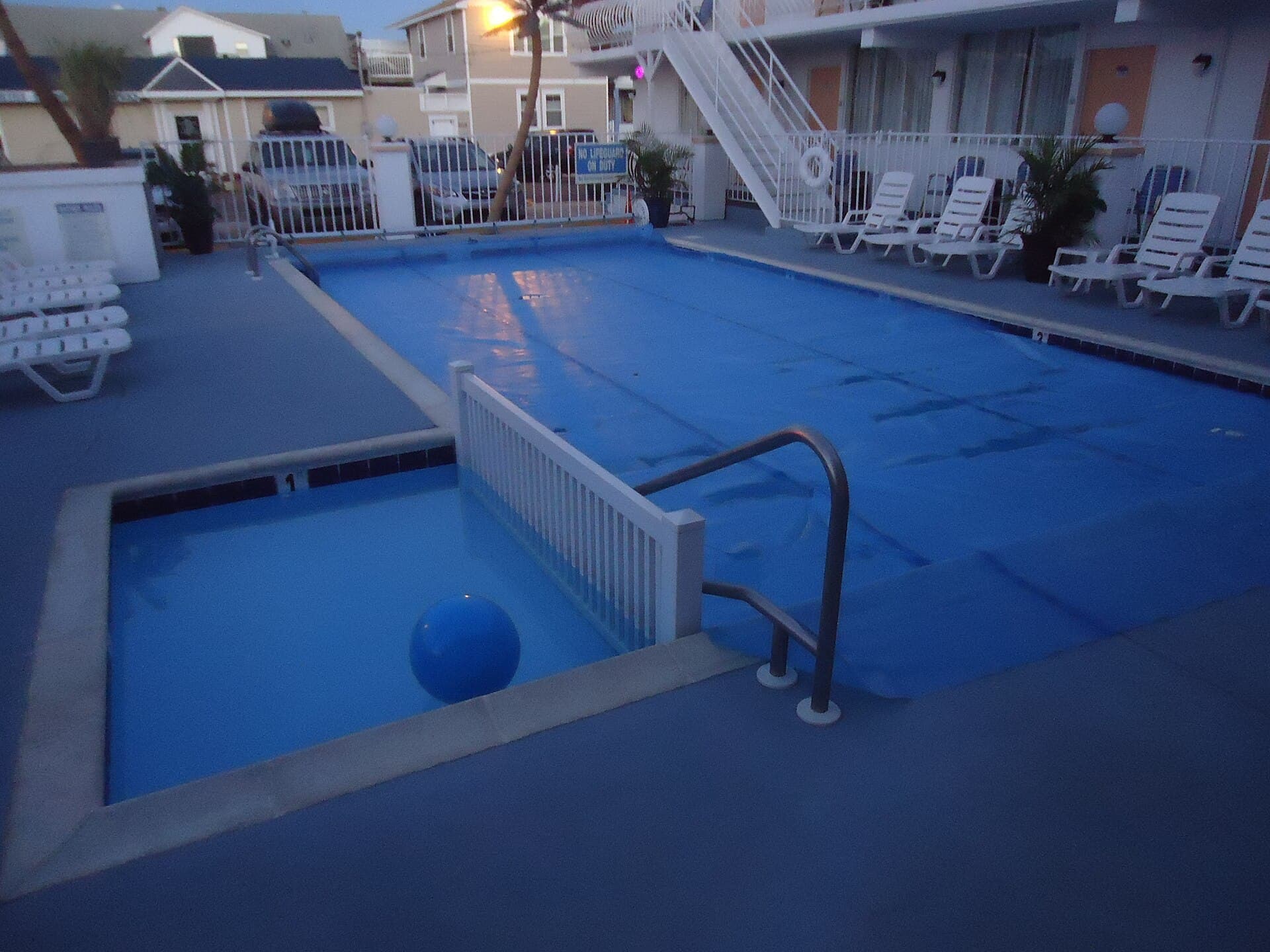 Aging motel swimming pool covered with a blue tarp at dusk, surrounded by dated lounge chairs and walkways