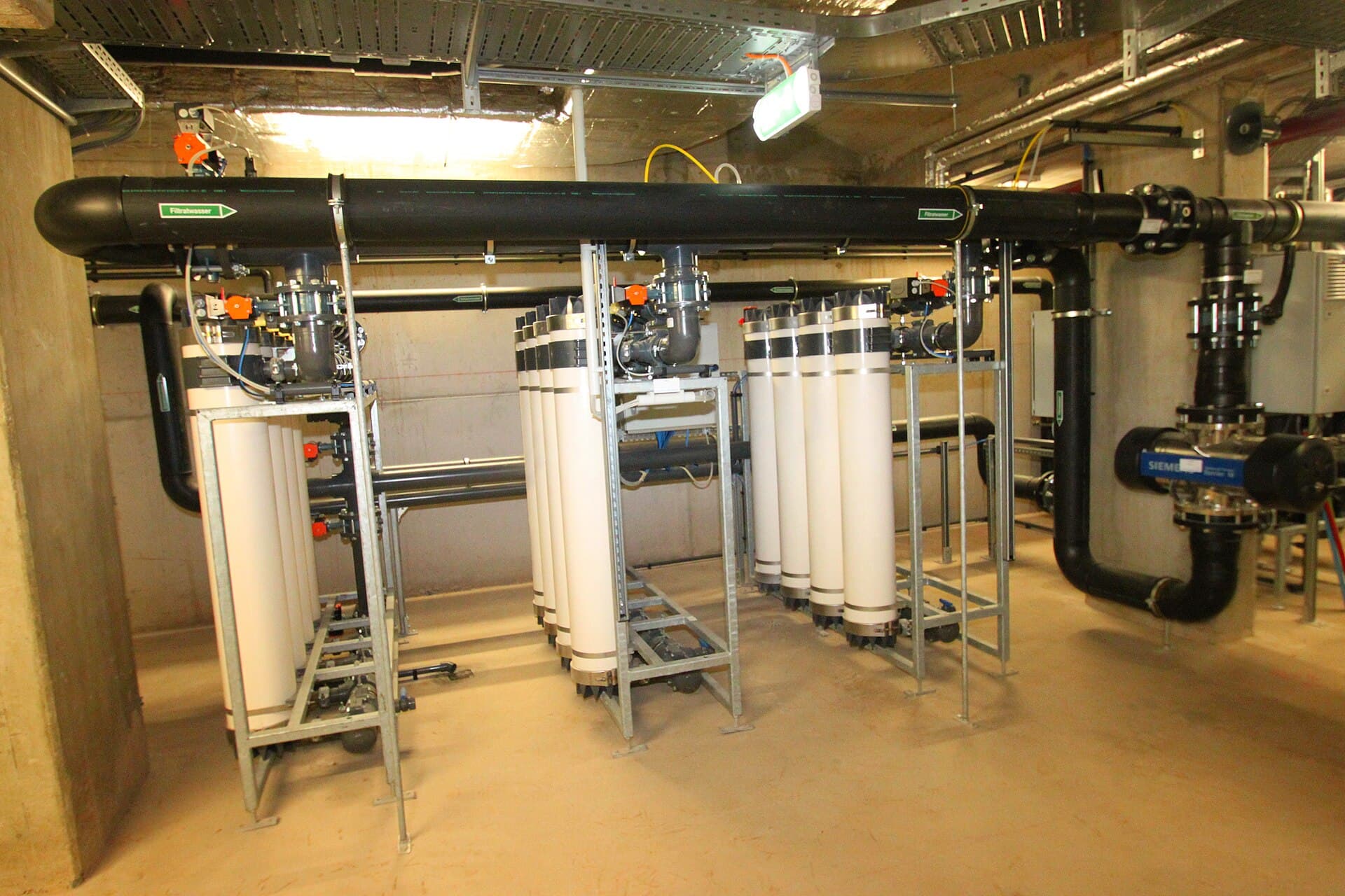 Swimming pool plant room with rows of filtration cylinders, pumps, and large water pipes