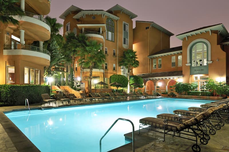 Amenity swimming pool at an apartment community at dusk, surrounded by lounge chairs and residential buildings