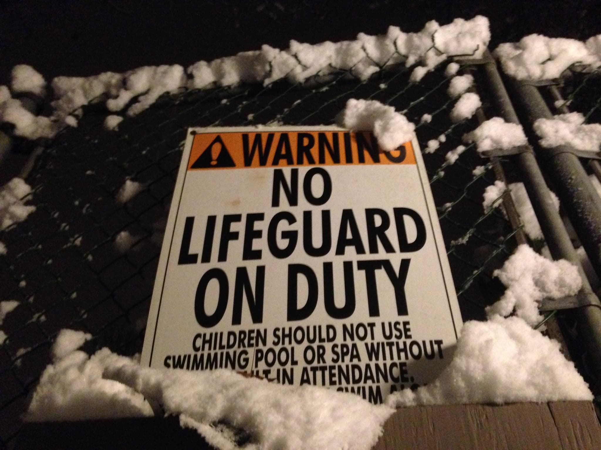 Warning sign on a pool fence reading 'No Lifeguard on Duty' with adult-supervision language
