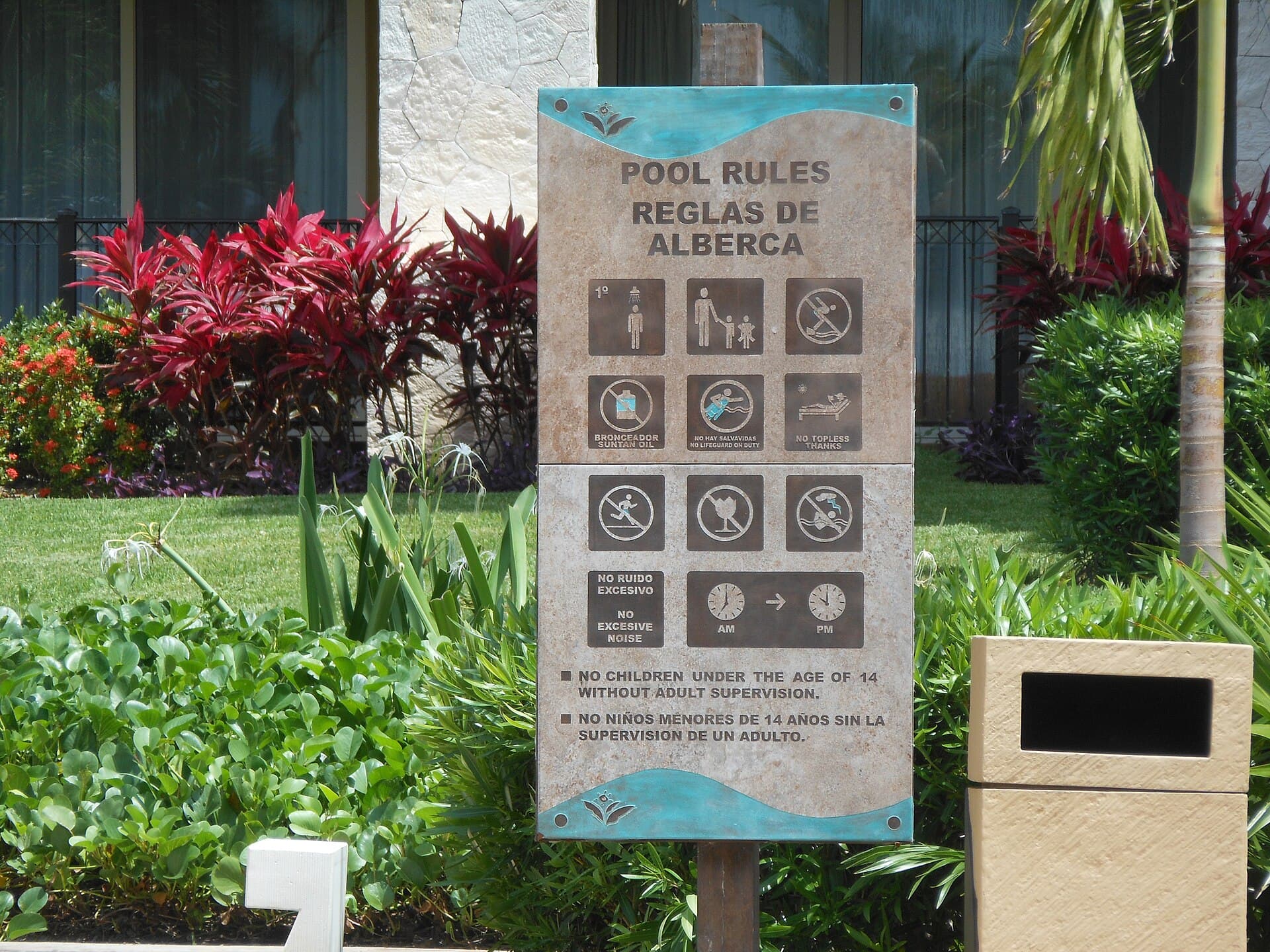 Bilingual English and Spanish pool rules sign with pictograms posted beside a swimming pool