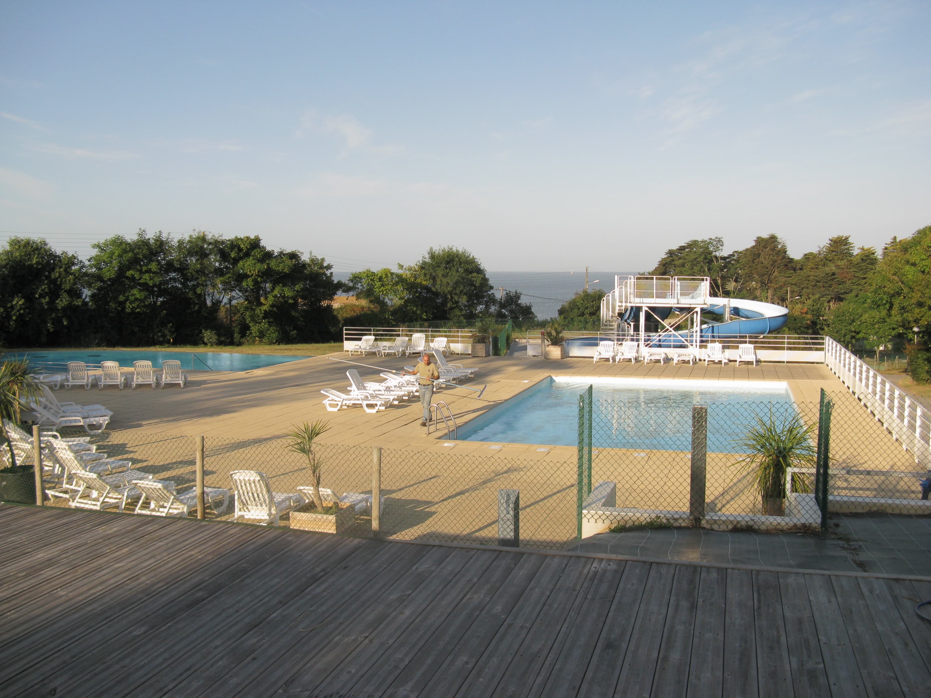 Technician performing early-morning maintenance with a telescopic pole at a large outdoor commercial pool