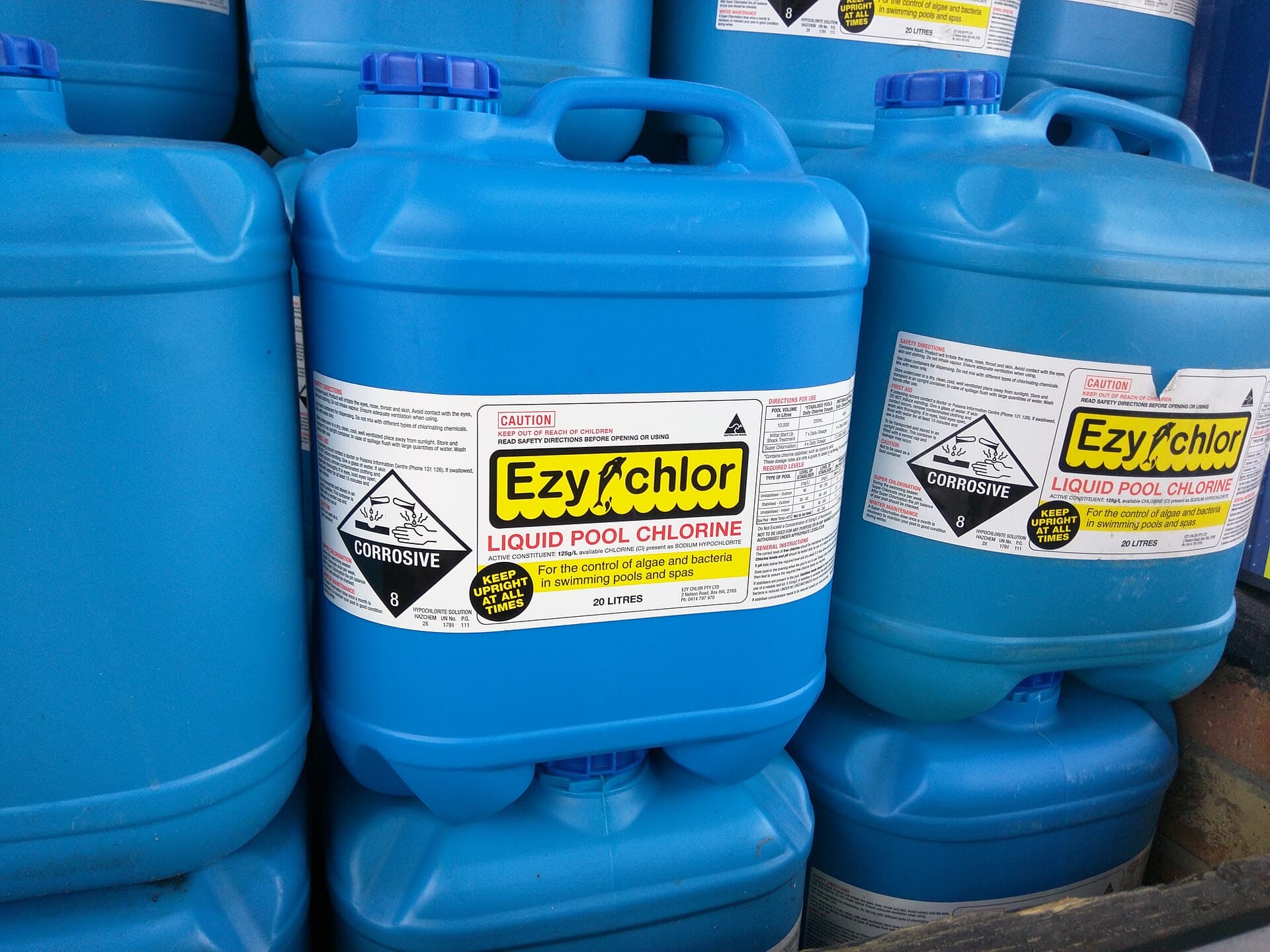 Stacked blue containers of liquid pool chlorine sanitizer for swimming pool water treatment