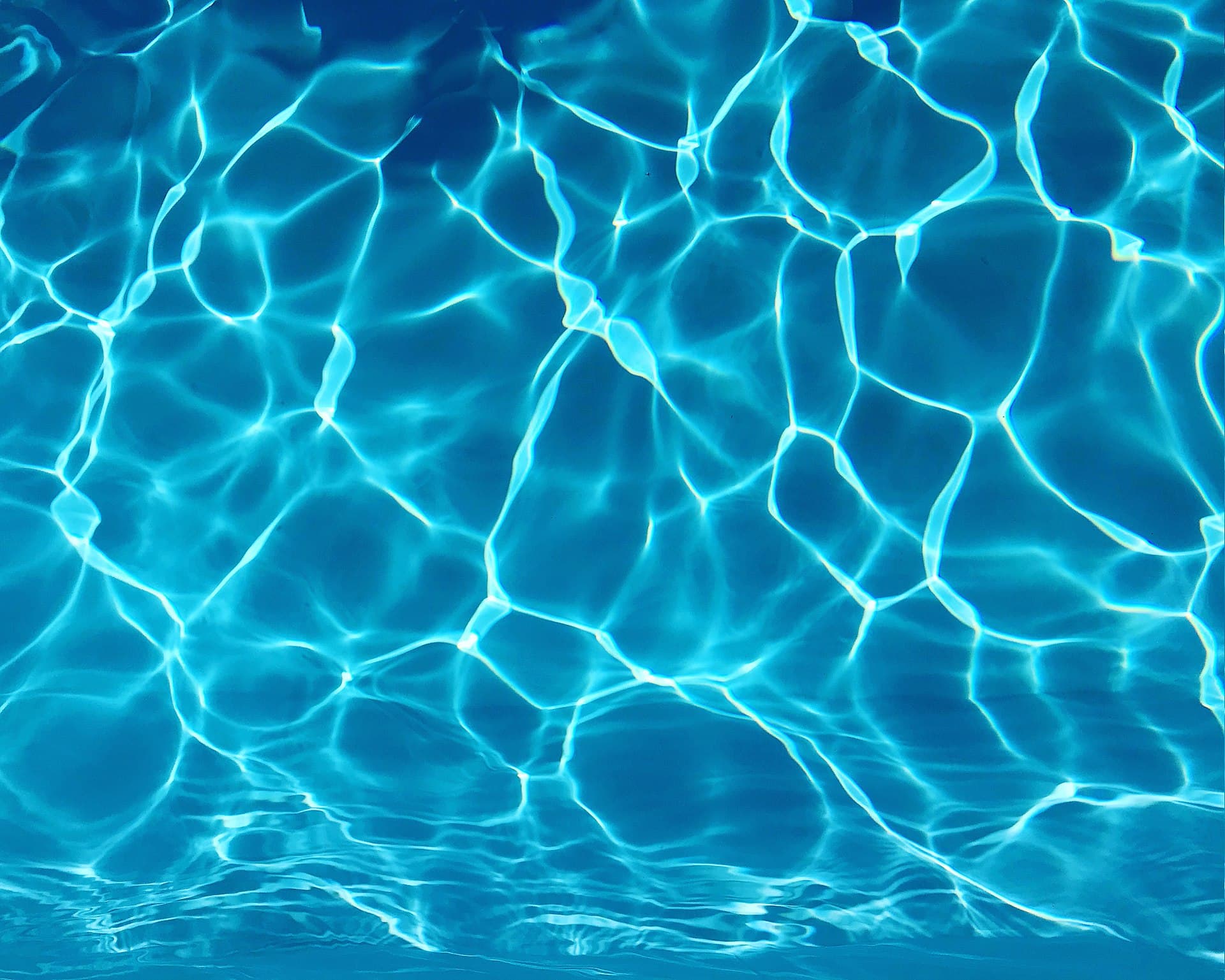 Sparkling clear blue swimming pool water with sunlight reflections rippling across the surface