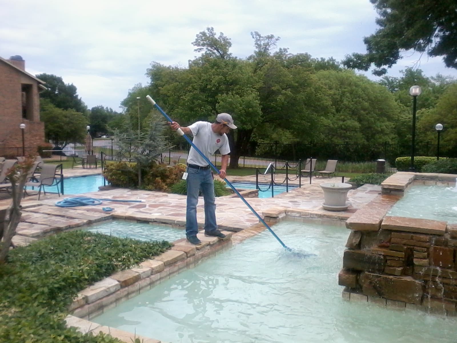 Pool maintenance technician cleaning a community pool with a vacuum head on a telescopic pole