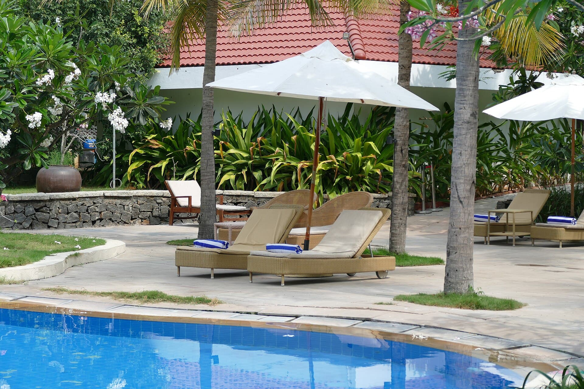 Resort poolside deck with wicker sun loungers and a white umbrella beside clear blue pool water