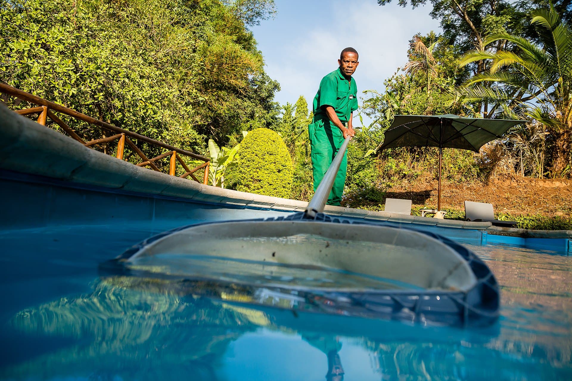 Pool technician skimming debris off blue pool water with a hand net on a telescopic pole