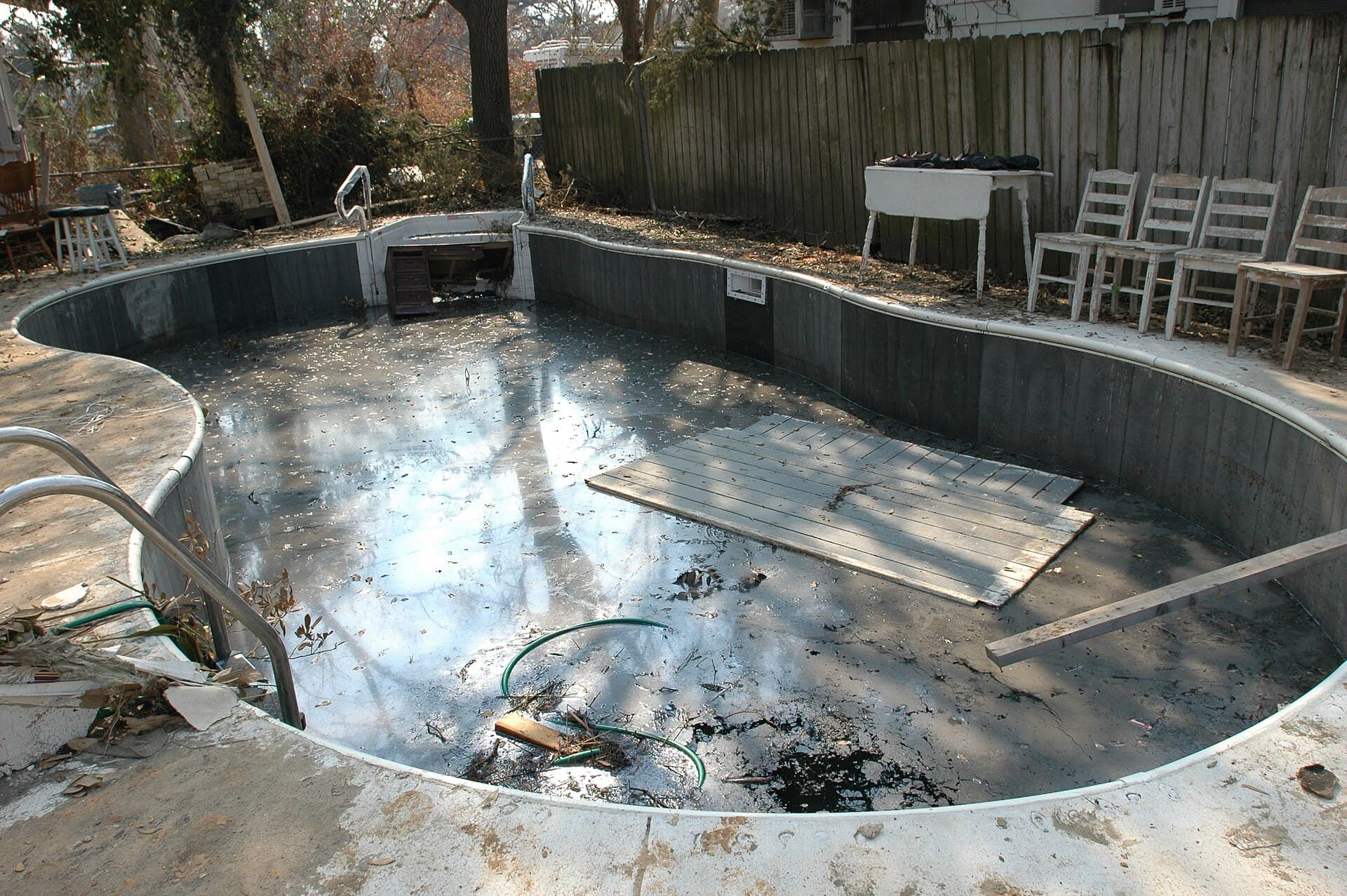 Backyard swimming pool filled with storm debris, mud and murky water after a major storm
