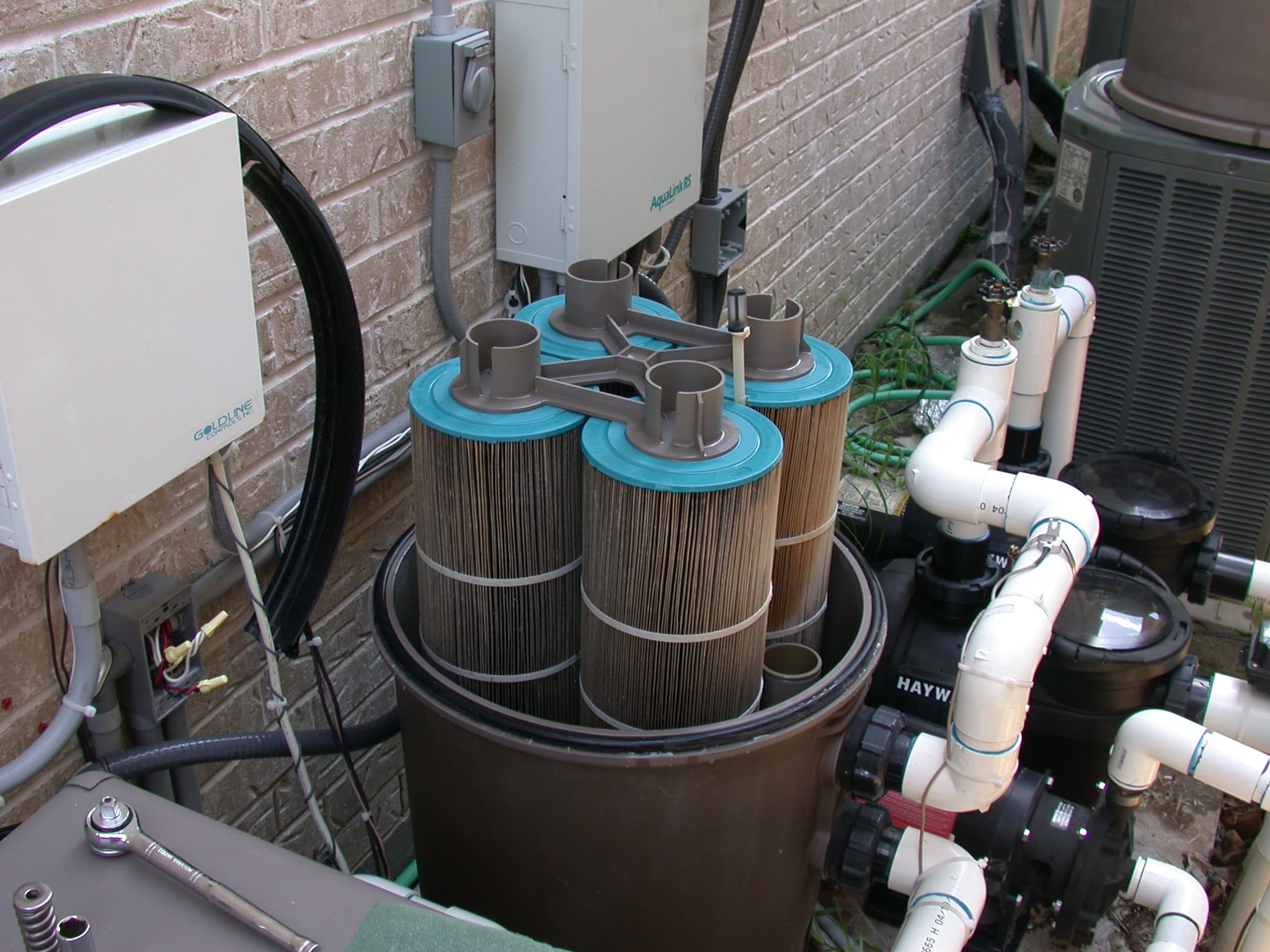Pool cartridge filter tank opened for service at an equipment pad, exposing the dirty filter cartridges