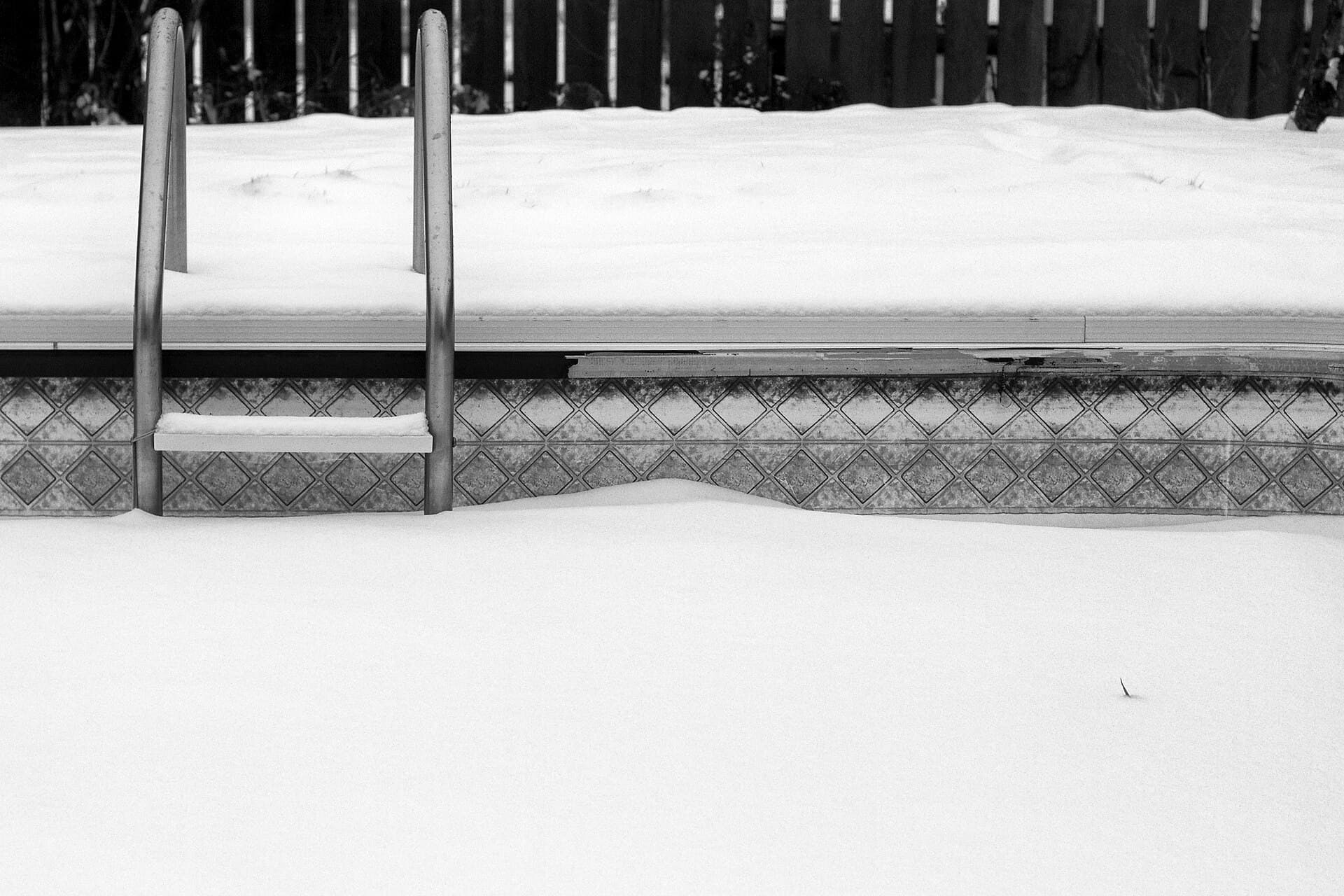 Swimming pool ladder buried in deep snow at a frozen backyard pool after a winter storm