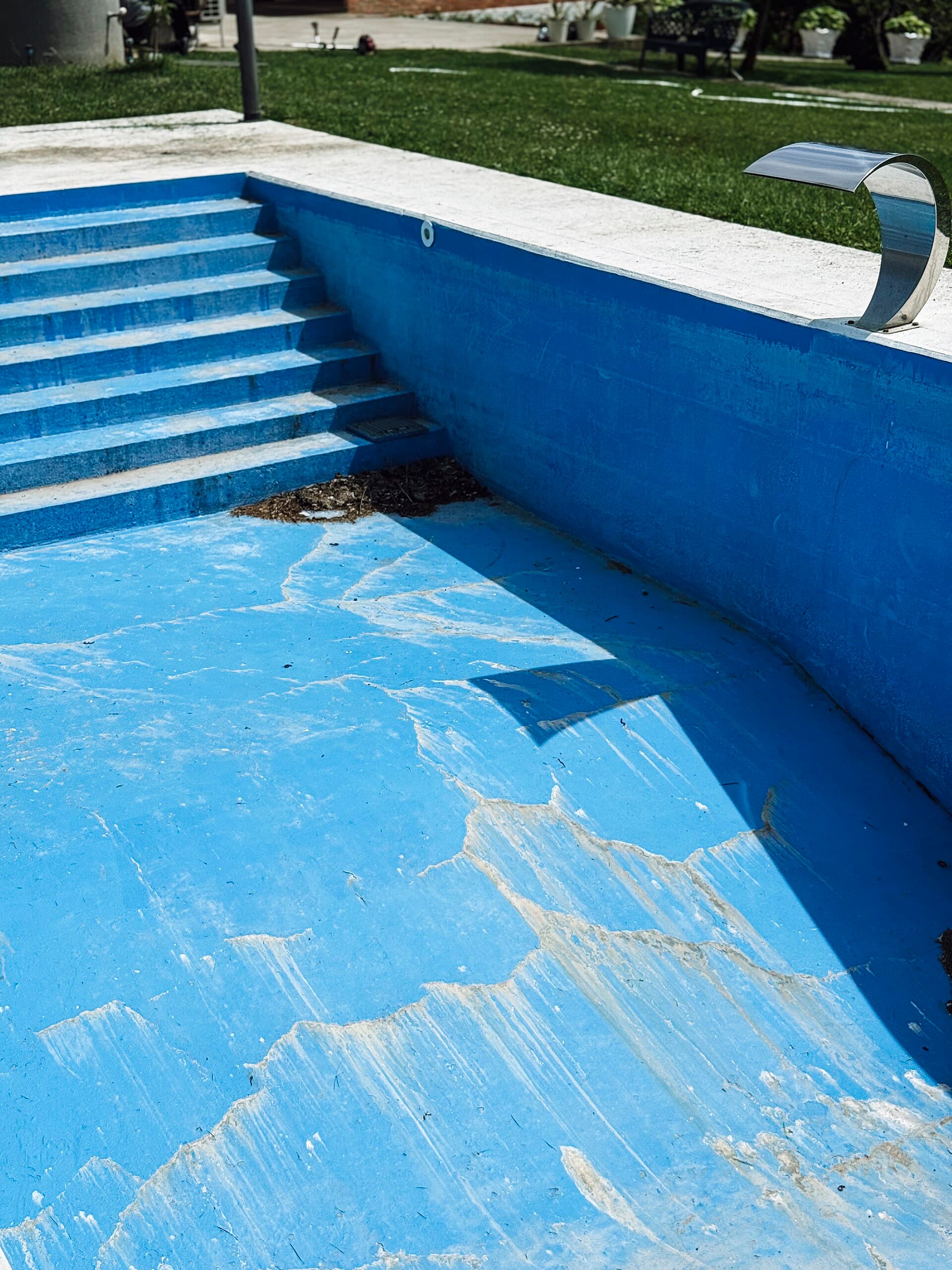 Drained backyard swimming pool with a faded blue finish showing cracks and stains across the shell