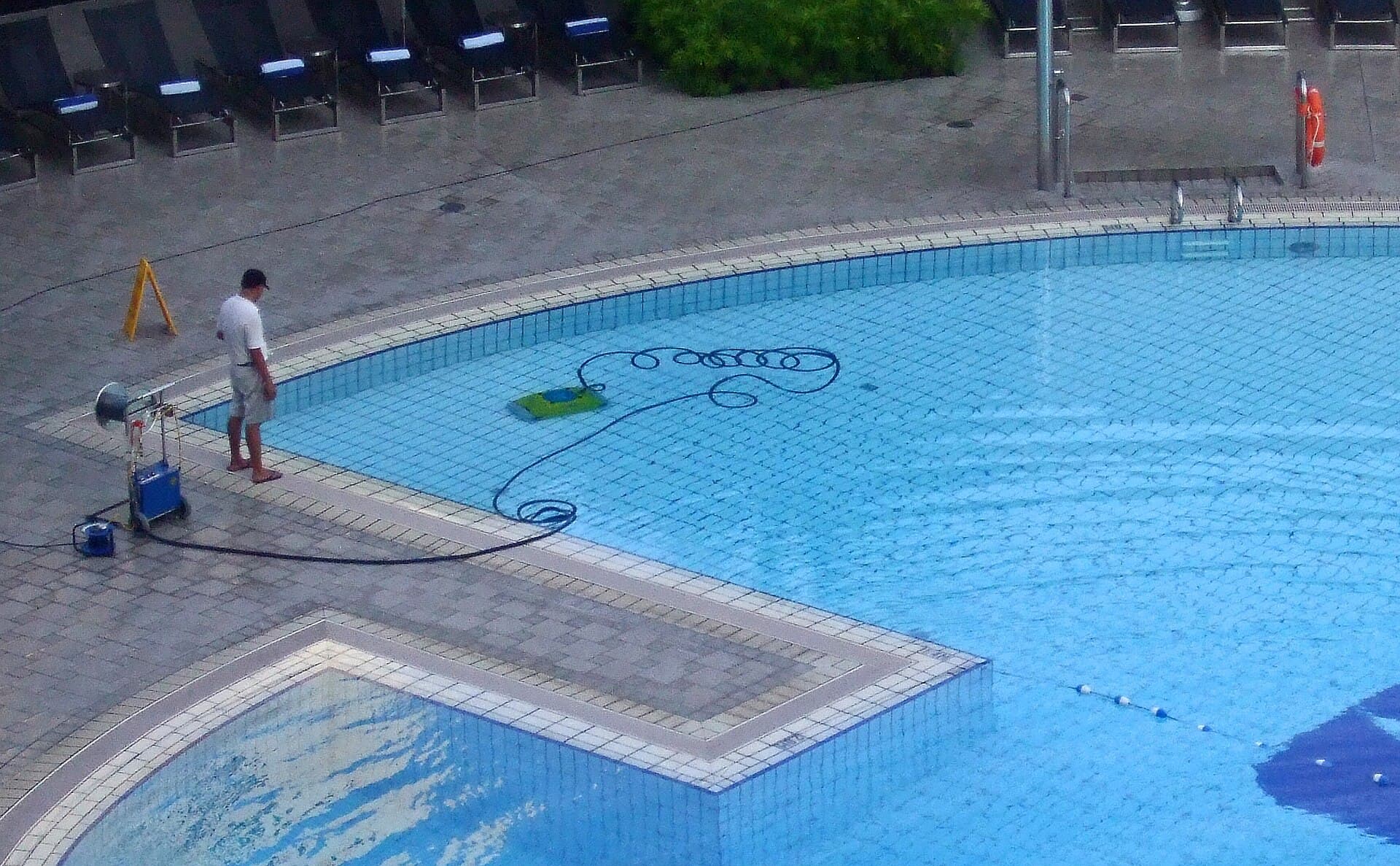 Pool technician watching a robotic pool cleaner work along the floor of a sparkling blue tiled swimming pool