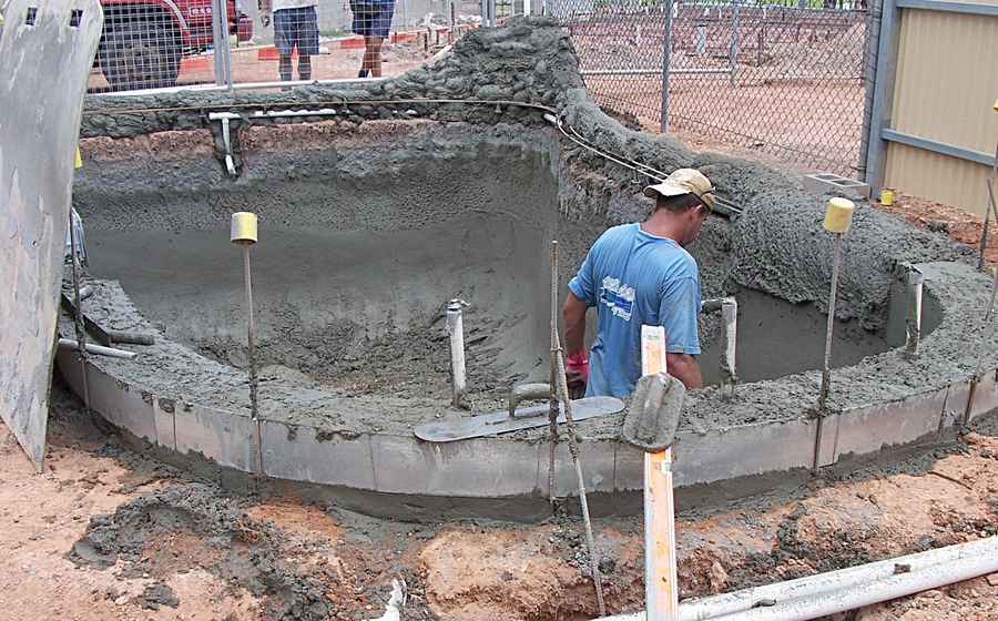 Worker shaping freshly sprayed shotcrete in a new swimming pool shell during construction